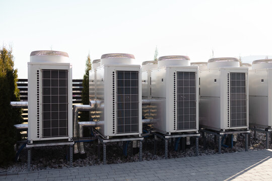 Multiple external industrial AC compressors and heat pumps installed outside a commercial building. Modern HVAC system, central air conditioning, and ventilation equipment concept.