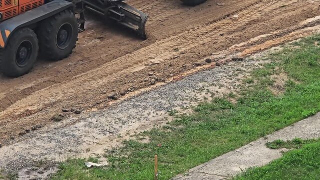 Heavy machinery road grader with large tires and blade levels dirt ground leaving tire tracks at construction site outdoors during day aerial view