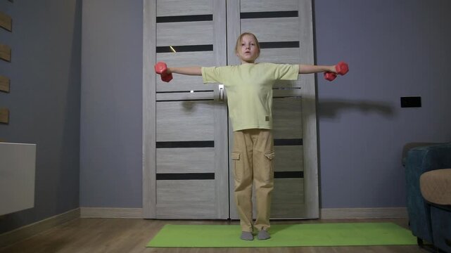 Young girl performing strength training workout with small dumbbells on yoga mat at home, engaging in fitness activity and physical exercise for health and wellness.
