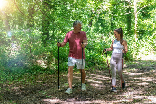 Senior man practicing Nordic walking with a professional fitness coach along a forest trail, improving walking technique, posture, endurance, coordination, 