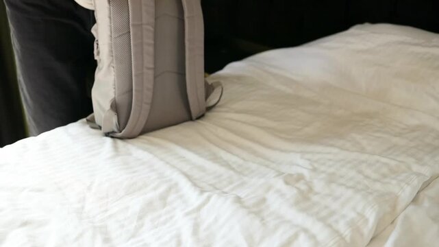 Close up of male hands neatly packing, closing, and zipping a grey textile travel backpack on a white bed. Preparing carry-on luggage for a weekend trip, summer vacation, or backpacking adventure in a