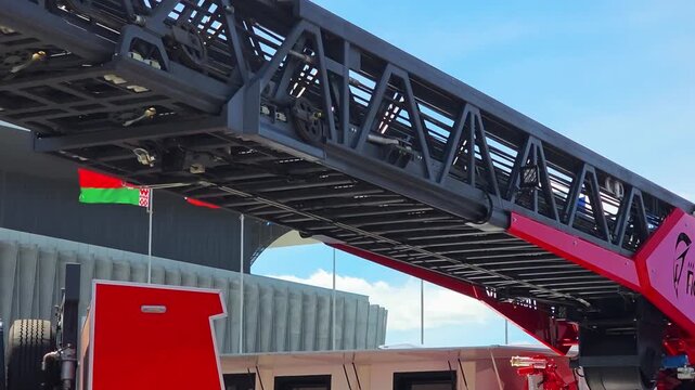 Extended telescopic ladder of a modern fire truck against a bright blue sky with white clouds, highlighting emergency rescue equipment and vehicle technology outdoors.