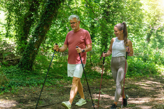 Nordic walking. Senior man practicing Nordic walking with a fitness coach on a forest trail to improve endurance, posture, balance, cardiovascular health, and overall functional mobility 