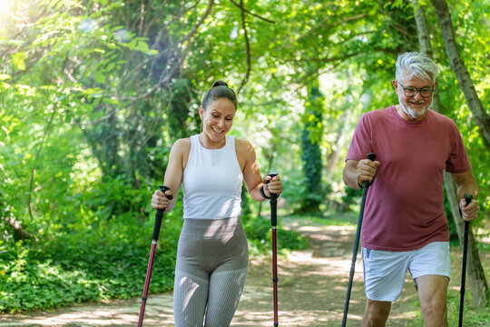 Senior man participating in a Nordic walking workout with instructor guidance to enhance cardiovascular endurance, walking mechanics, posture, coordination, and functional fitness outdoors.