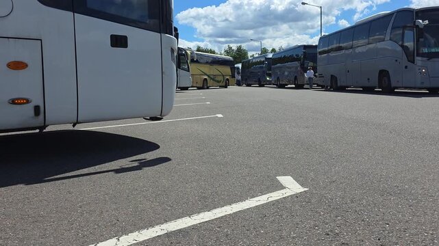Multiple tour buses parked in large asphalt parking lot under bright blue sky with white clouds on sunny day, illustrating transportation infrastructure for travel and tourism industry