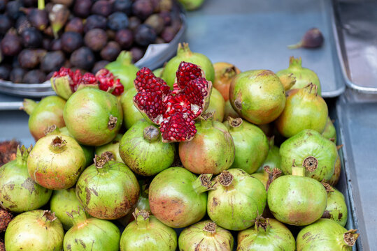 Fresh Green Pomegranates With One Ripe Open Fruit Displayed at Traditional Market Stall