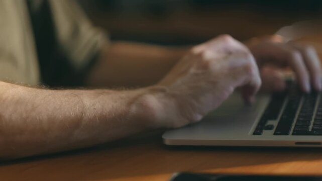 Closeup man hands multitasking at desk, switching from using smartphone, typing on laptop keyboard in sunlit room, illustrating modern work, communication concepts. Man use smartphone typing on laptop
