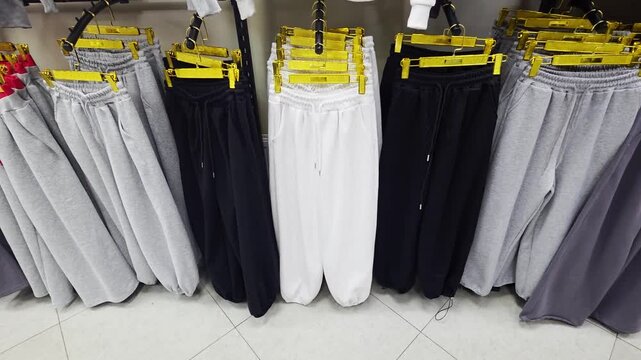 Assortment of comfortable casual sweatpants and joggers displayed on clothing rack in retail store showcasing various colors and styles for sale, from pink to grey to black and white.