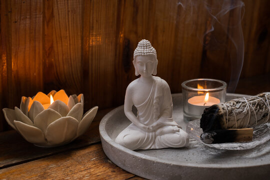 White Buddha statue with burning candles and sage smudge stick for meditation and spiritual cleansing concept	