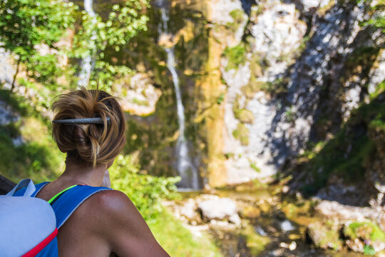 Rear view of a female hiker with a backpack looking at a mountain waterfall in the blurred background in Austria