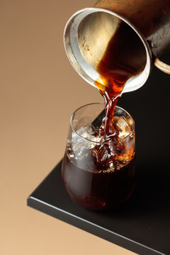 Black coffee is poured into a glass with ice.