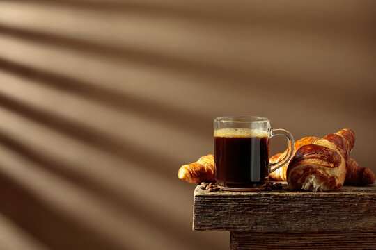 Black coffee with croissants on an old wooden table.