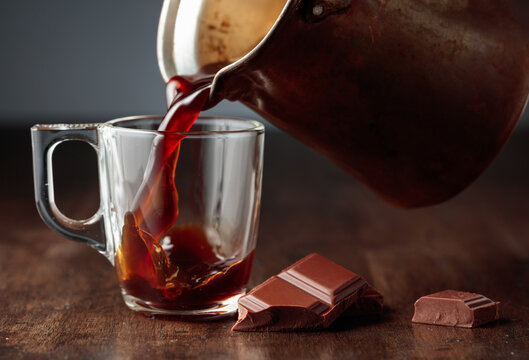 Black coffee is poured into a glass cup.