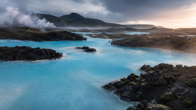 Turquoise Geothermal Lagoon With Steam Rising Off Dark Volcanic Rock Formation Landscape