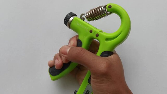 A person squeezes a green hand gripper spring tool to build forearm strength and improve grip power effectively