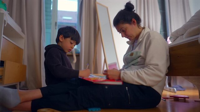 Mother and school age son draw together on bedroom floor at home, encouraging creativity, imagination, family bonding and positive childhood development