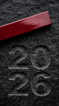 Carved number 2026 on dark textured surface with a red glossy element, representing a date or year with a modern contrast, suitable for time or event themes