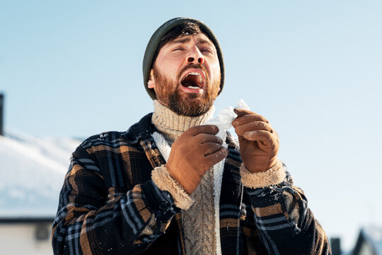 Bearded man sneezing cold illness in winter outdoor