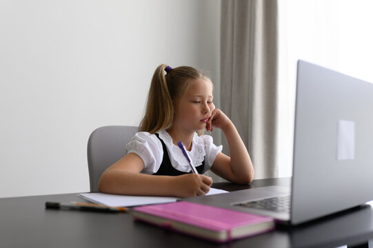 Bored schoolgirl resting head on hand during dull online lesson