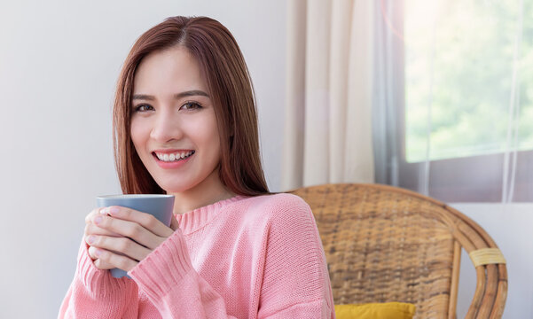 Portrait of young beautiful asian woman in sweater hands holding a cup of marsh mellow coffee morning winter time relax at home. Happy cheerful relaxing cold winter, barista lifestyle, holiday banner