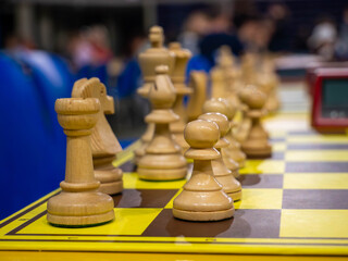 Close up of white wooden chess pieces on chessboard with blurred background at tournament © YULIIA