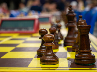 Close up of dark wooden chess pieces on chessboard with blurred background at tournament © YULIIA