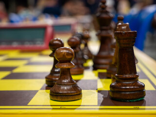Close up of dark wooden chess pieces on chessboard with blurred background at tournament © YULIIA