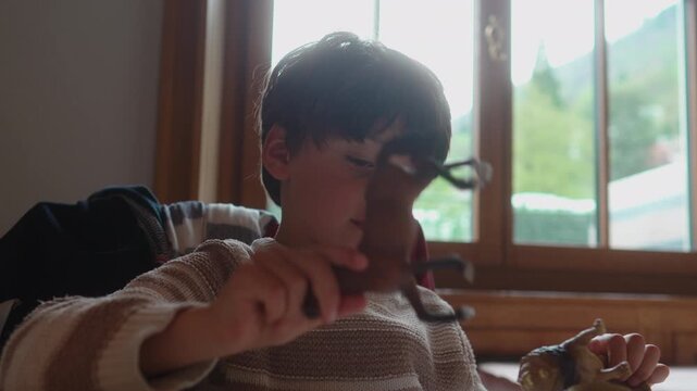 School age boy taps toy on restaurant table while waiting for meal, expressing mild boredom, imaginative self entertainment, family outing and authentic childhood behavior