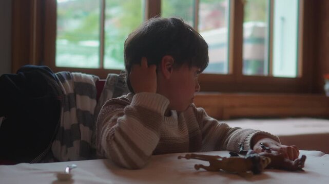 School age boy waits at restaurant table while absentmindedly scratching his head, expressing mild boredom, family dining and authentic childhood patience
