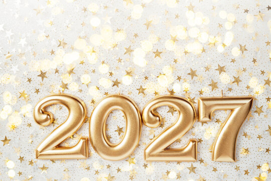 Holiday background Happy New Year 2027. Numbers of year 2027 made by burning gold candles on red festive sparkling background.