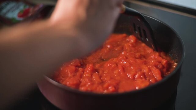 A person is stirring a tomato sauce in a pan on a stovetop. The scenario showcases the preparation of a dish in a kitchen setting