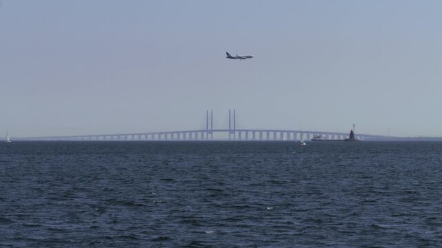 Wide view of Oresund Bridge (Oresundsbron) and airplane flying overhead, Denmark
