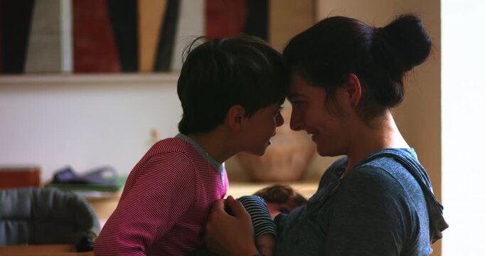 Mother and young son touch foreheads in playful moment at home, celebrating emotional closeness, secure attachment and joyful family connection