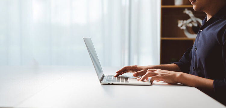 Person typing on modern laptop keyboard, engaging in professional work remotely, writing email, coding, or learning online in a bright home office setting