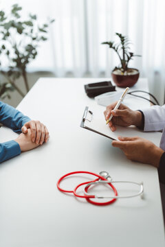 Doctor's hands writing on a medical clipboard during a consultation with a patient, discussing examination, diagnosis, and treatment plan in a healthcare setting