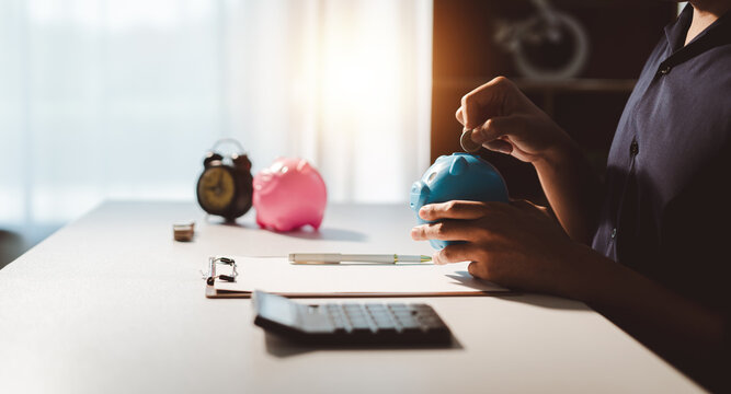 Person placing a coin into a blue piggy bank, demonstrating financial planning, wealth accumulation, long term investment, and saving money for future goals and retirement