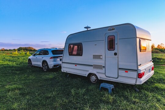 Camper trailer parked on green grass during sunset with a silver SUV nearby