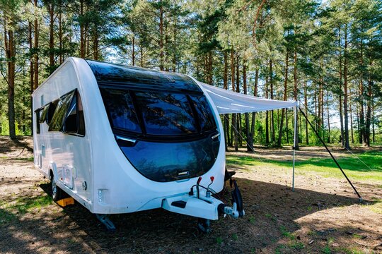 Camper trailer parked under trees with awning extended in bright sunlight