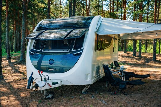 Travel trailer exterior with awning and chairs in a serene forest setting