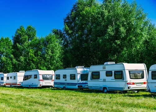 Row of parked white caravans surrounded by lush greenery under a clear blue sky