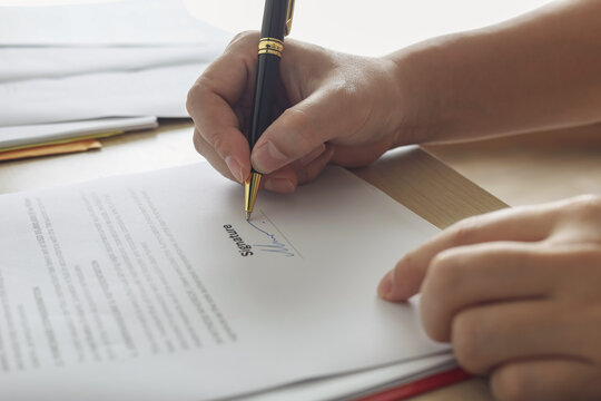 Close up of hand signing signature on business contract document with pen. Concept of deal agreement, legal document, and approval.
