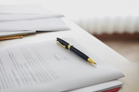 Luxury pen placed on signed business contract document on desk. Concept of approved deal, legal agreement, and completed transaction.