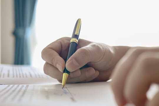 Close up of hand signing signature on business contract document with pen. Concept of deal agreement, legal document, and approval.