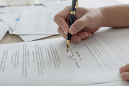 Close up of hand signing signature on business contract document with pen. Concept of deal agreement, legal document, and approval.