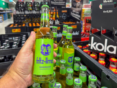 Berlin, Germany July 29, 2026. A hand holds a green labeled fritz limo soda bottle flavored with honeydew melon at a store. More bottles of this German soft drink fill a crate in the blurred backgroun