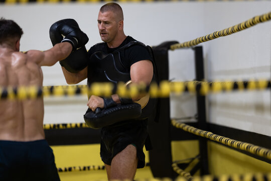 Boxer Training With Coach In Boxing Ring During Focus Mitt And Body Armor Drills