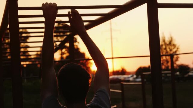 Athletic man performing pull ups on monkey bars at sunset outdoor fitness.