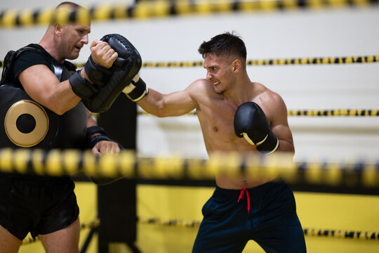Young Boxer Sparring With Trainer Using Punch Pads In Boxing Gym Training Session