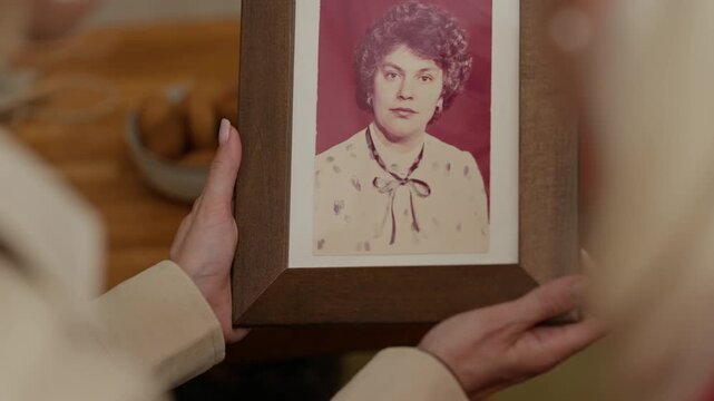 Middle aged Caucasian woman holding vintage framed portrait of young woman and holding hands with senior mother. Clip is ideal for senior care, family heritage, or memory care marketing