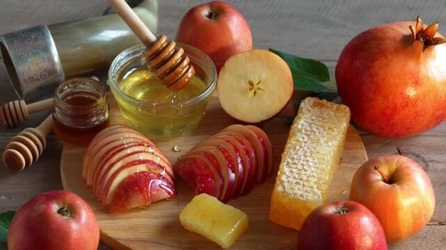 Happy Rosh Hashanah. Jewish New Year holiday concept. Honey dipper dripping honey to apples slices, next to apples, shofar horn and pomegranates.